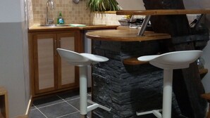 A kitchen with a stone accent wall, wooden cabinets, a sink, and two bar stools. - Apartment La Musette Historic Center of Dijon (Dijon)
