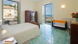 Un dormitorio con cama, armario, banca y vista al mar desde un balcón.