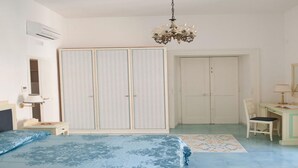 A bedroom with a large bed, a desk, a chair, a wardrobe, and a chandelier.