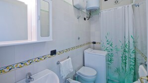 Une salle de bain équipée de toilettes, d’un bidet, d’un lavabo et d’un rideau de douche orné d’un motif en bambou.
