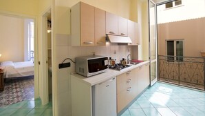 Une cuisine compacte équipée d’un four à micro-ondes, d’une cuisinière et de placards. On aperçoit un petit coin repas, avec un lit en arrière-plan.