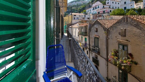 Un balcon avec une chaise bleue, donnant sur une colline parsemée de bâtiments dotés de balcons et de plantes en pot.