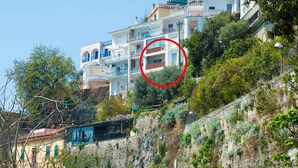 Un edificio en una ladera con varios balcones, un muro de piedra de contención y un cielo despejado.