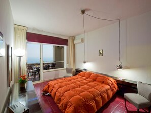 Une chambre d’hôtel équipée d’un lit, d’un bureau, d’une chaise, d’une fenêtre donnant sur un paysage agréable et d’un balcon.