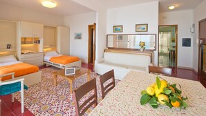 Una habitación de hotel compacta con dos camas, una kitchenette pequeña, un comedor con una mesa y sillas, y una sala de estar con un sofá.