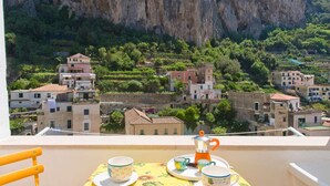 A balcony with a table set for two, overlooking a village with terraced houses and a cliff. - Appartamento a Amalfi ID 3062 (Amalfi)