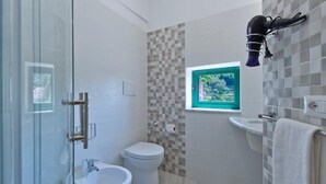 A bathroom with a glass shower enclosure, a bidet, a toilet, and a small window with a view.