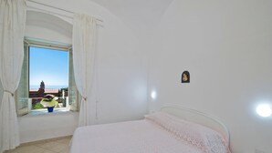 A bedroom with a bed, a window with curtains, a small wall-mounted decoration, and a view of buildings and a tower outside.