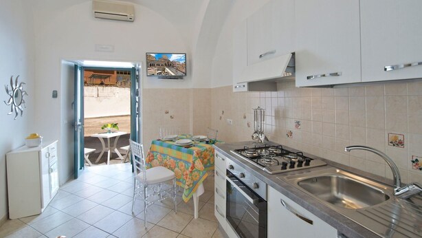 A compact kitchen with white cabinets, a gas stove, a sink, and a dining area with a table and chairs.