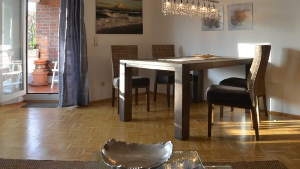 Comedor con mesa de madera, sillas y una araña. Se aprecia un camino de mesa de vidrio con un cuenco decorativo.