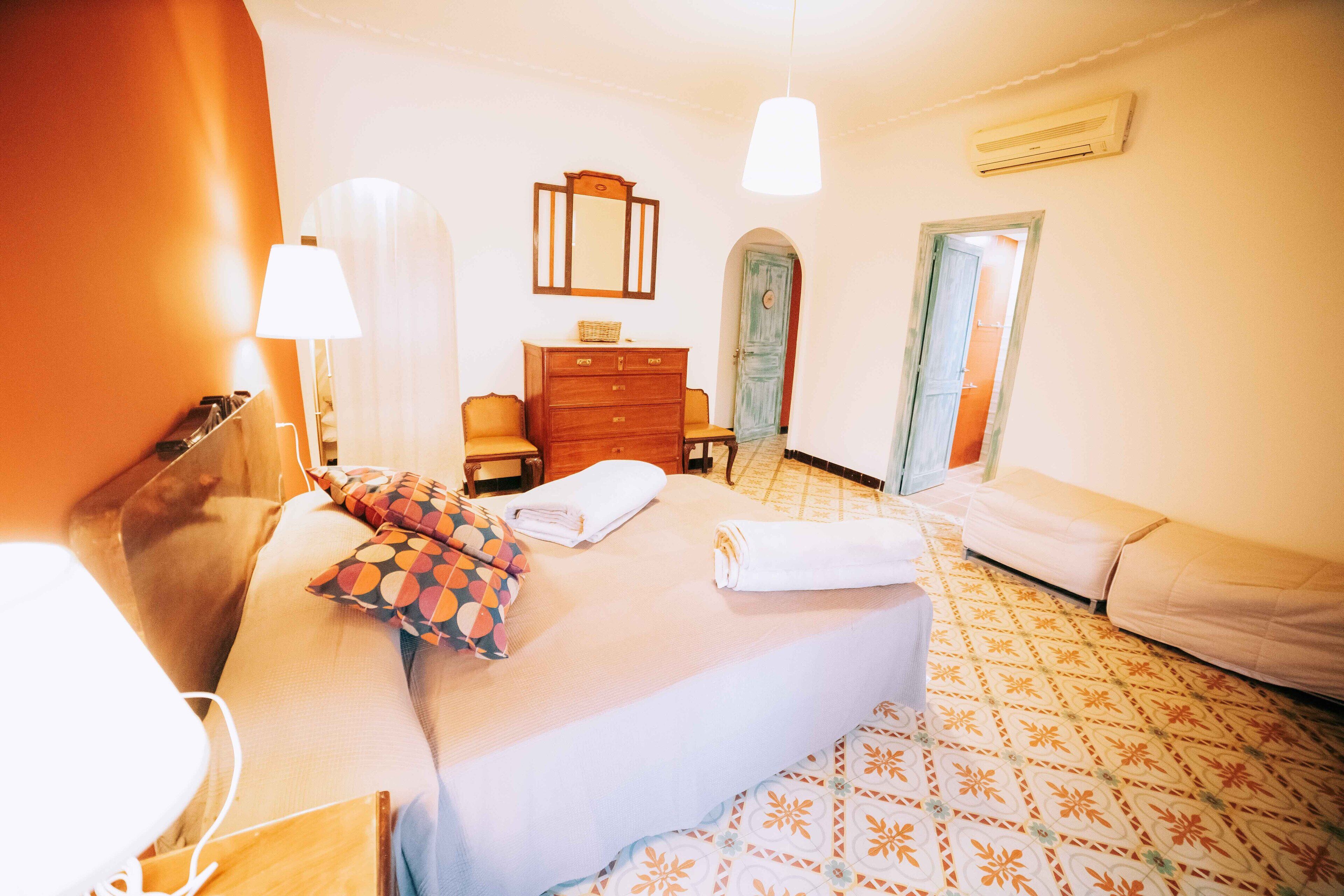 Una habitación de hotel con cama, cómoda, espejo, lámpara y puerta que da a otra habitación.