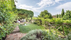 Un jardín rústico con un pérgola, mobiliario exterior y un sendero de ladrillo.