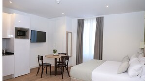 Une chambre d’hôtel de taille réduite, comprenant un lit, une petite table à manger avec des chaises, un four à micro-ondes et un téléviseur.