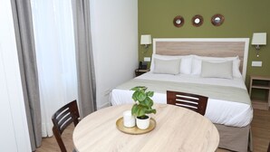 Une chambre d’hôtel bien rangée, avec un lit, des lampes de chevet, une table ronde en bois ornée d’une plante et une chaise.