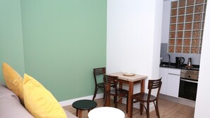 A small, compact living space with a kitchenette, a dining area with a table and chairs, and a sofa with a yellow pillow. - Exterior studio for 3 people (Madrid)