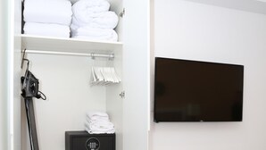 A hotel room with a neatly organized closet containing folded towels, a hairdryer, and a storage box. A flat-screen TV is mounted on the wall, and a bed with a green patterned bedspread is visible. - Exterior studio for 3 people (Madrid)