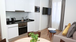 A compact living space with a kitchenette, a dining area, and a seating area with a TV mounted on the wall. - One bedroom exterior apartment with two balconies for 4 people (Madrid)