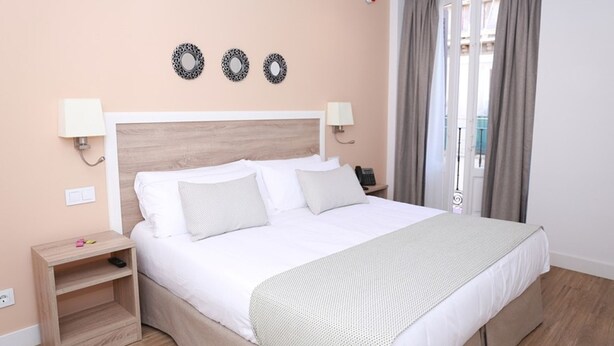 A hotel room with a bed, bedside tables, a lamp, and a view of the outside. - One bedroom exterior apartment with two balconies for 4 people (Madrid)