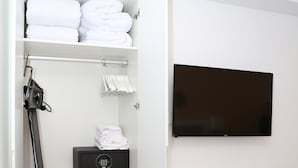 A hotel room with a neatly organized closet containing folded towels, a hairdryer, and a storage box. A flat-screen TV is mounted on the wall, and a bed with a green patterned bedspread is visible. - One bedroom exterior apartment with two balconies for 4 people (Madrid)