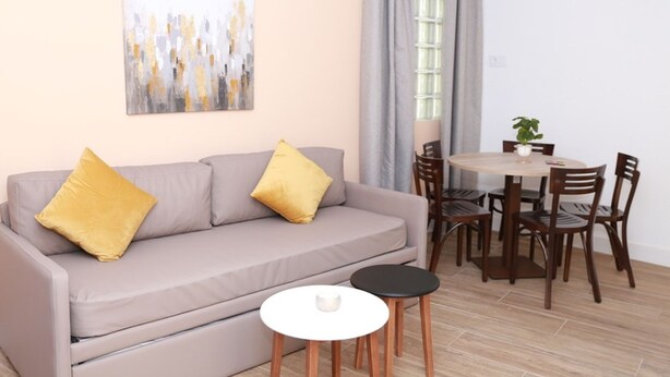 A living room with a grey sofa, two yellow cushions, a round white coffee table, and a dining area with wooden chairs and a round table.