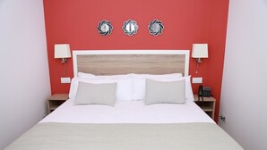 A bed with white bedding, two pillows, a wooden headboard, and a red wall with three decorative wall stickers.