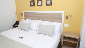 Ein ordentlich bezogenes Bett mit weißen Leinentüchern und zwei Kissen, ein Nachttisch mit Lampe und ein an der Wand befestigtes Telefon.