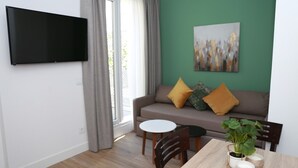 A modern living room with a flat-screen TV, a green accent wall, a sofa with cushions, a dining table with chairs, and a potted plant. - One bedroom penthouse with terrace for 4 people (Madrid)
