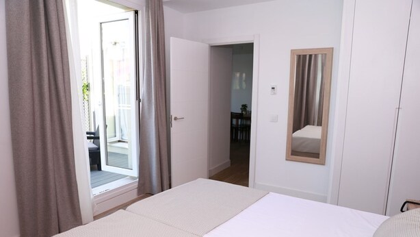 A hotel room with a bed, a door leading to a balcony, and a mirror on the wall. - One bedroom penthouse with terrace for 4 people (Madrid)