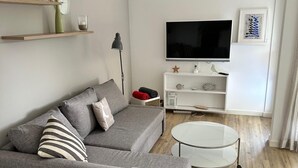 A modern living room with a grey sofa, a round coffee table, and a flat-screen TV on a white stand. - Duck nest at the village pond (Wenningstedt-Braderup (Sylt))