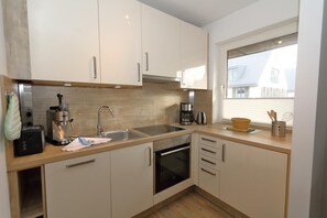 Een moderne keuken met witte kastjes, roestvrijstalen apparatuur en een raam dat voor natuurlijk licht zorgt.