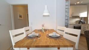 A dining area with a wooden table set for four, white chairs, and a white pendant light. - Duck nest at the village pond (Wenningstedt-Braderup (Sylt))