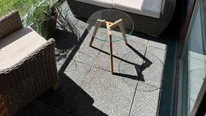 A balcony with wicker furniture, a glass table, and a view of a brick building and greenery. - Duck nest at the village pond (Wenningstedt-Braderup (Sylt))
