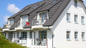 A multi-story residential building with a sloped roof, multiple windows, and a balcony with outdoor furniture. - Apartment Filter, Germany (Hörnum (Sylt))