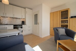 Um espaço compacto com cozinha compacta, sofá, mesa de jantar e armário com copos.