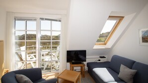 A modern living room with a TV, sofa, and a view of outdoor seating through large windows. - Apartment Filter, Germany (Hörnum (Sylt))