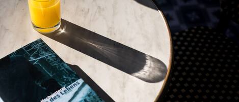 A glass of orange juice on a marble table next to a book titled "Die Suite des Lebens".