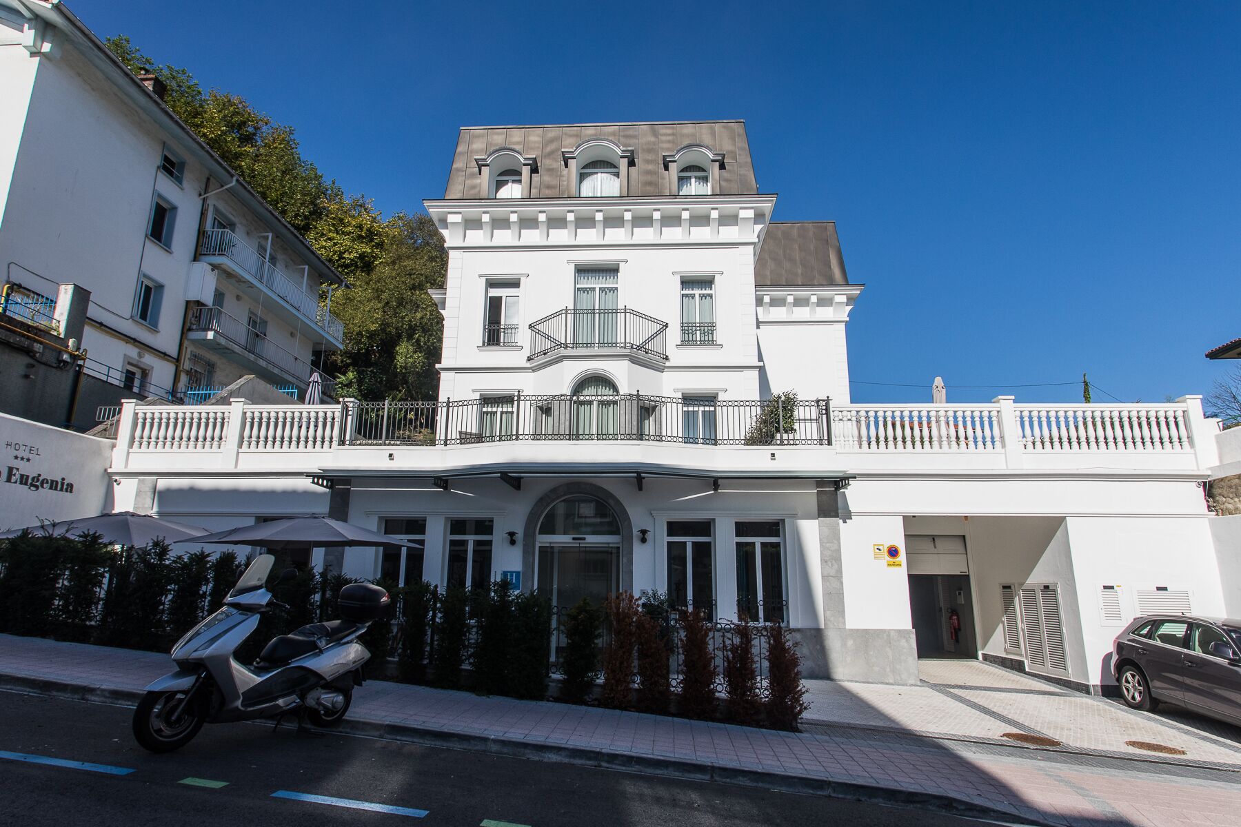 A two-story building with a balcony, a door, and a small parking area.