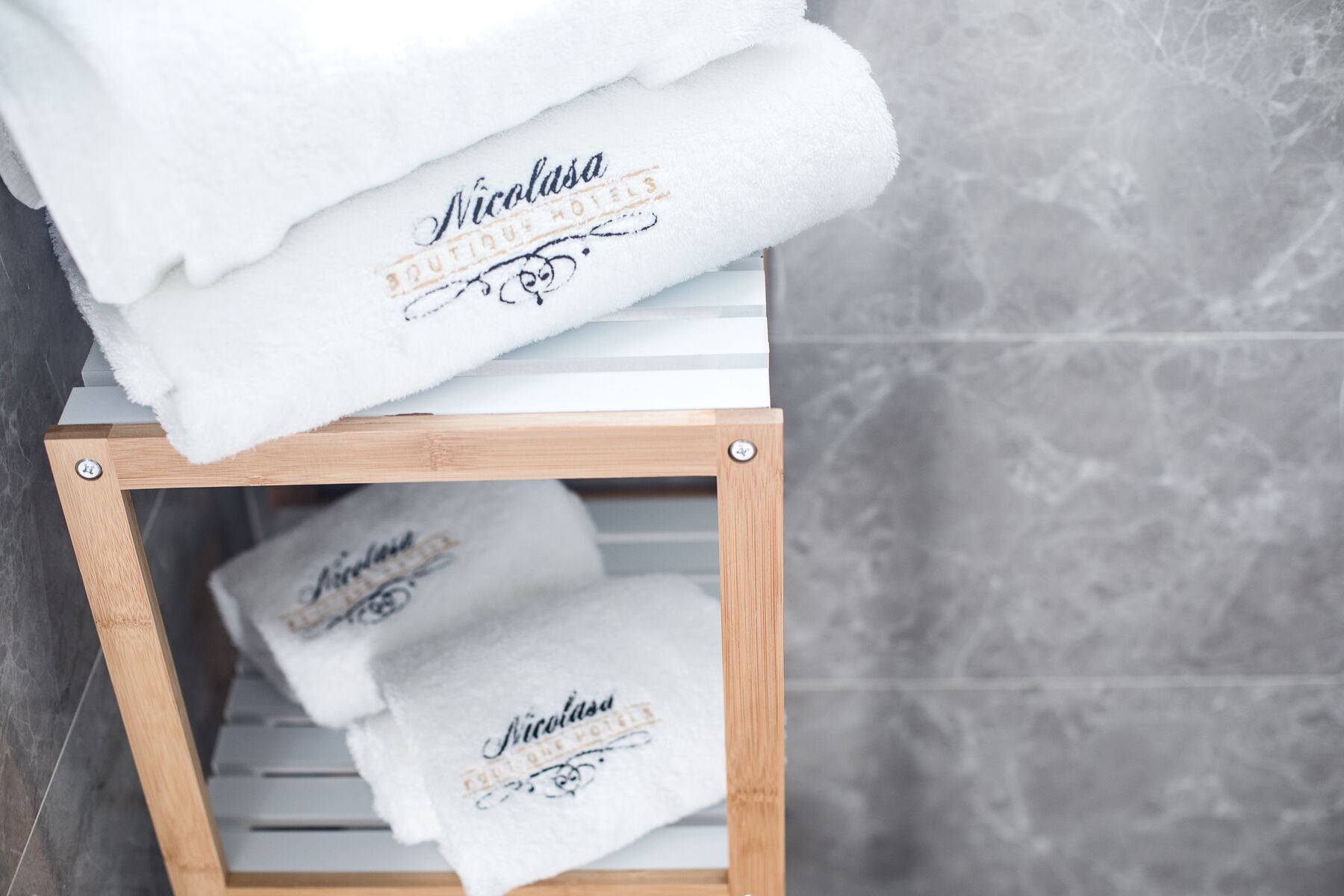 A wooden shelf with folded white towels stacked on top and placed on the shelf.