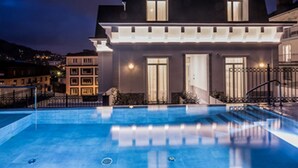 Un hotel moderno con una amplia piscina al aire libre, una entrada bien iluminada y vistas de la ciudad circundante.
