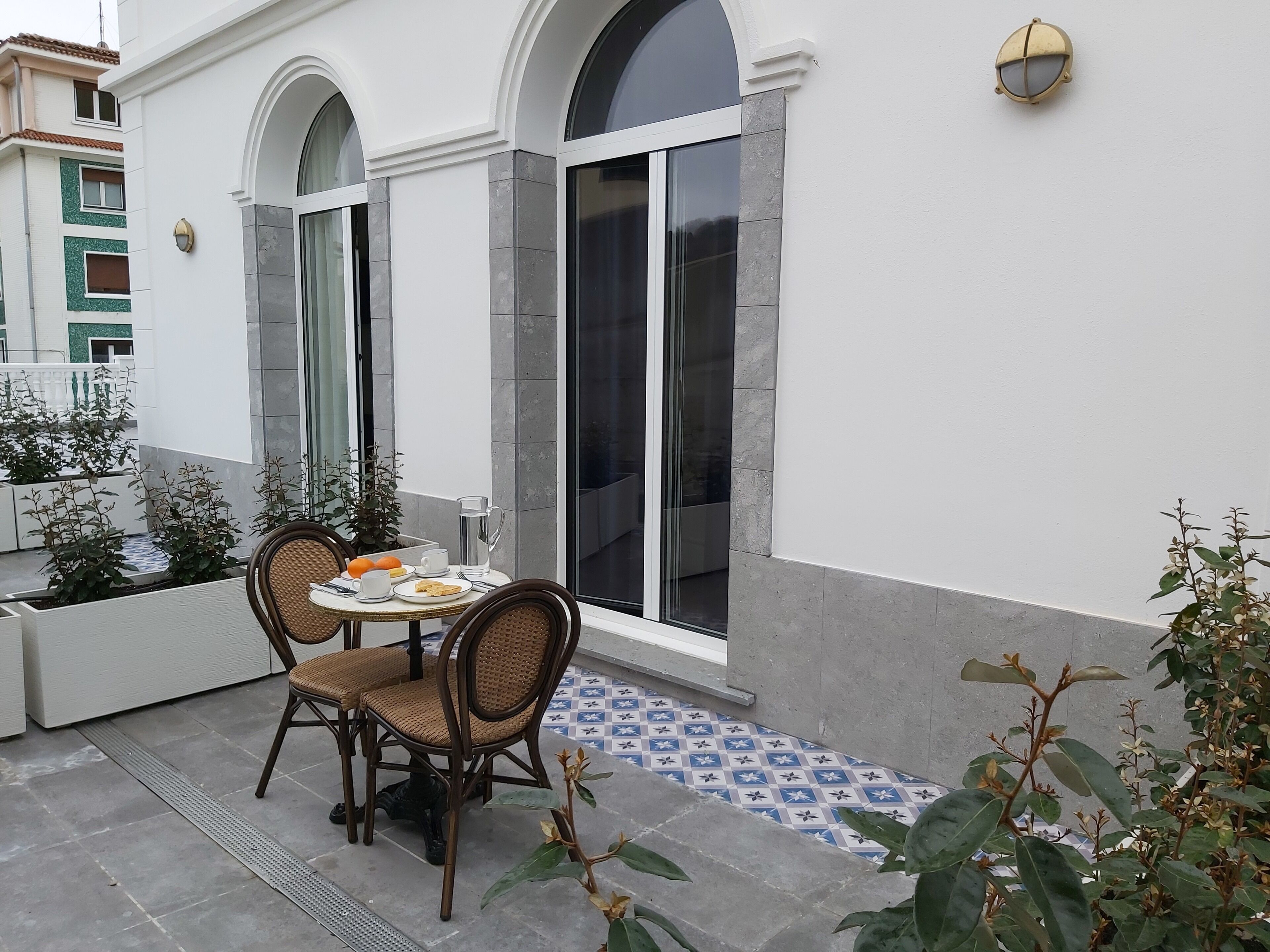 A patio with a round table and four wicker chairs, a small potted plant, and a tiled floor.