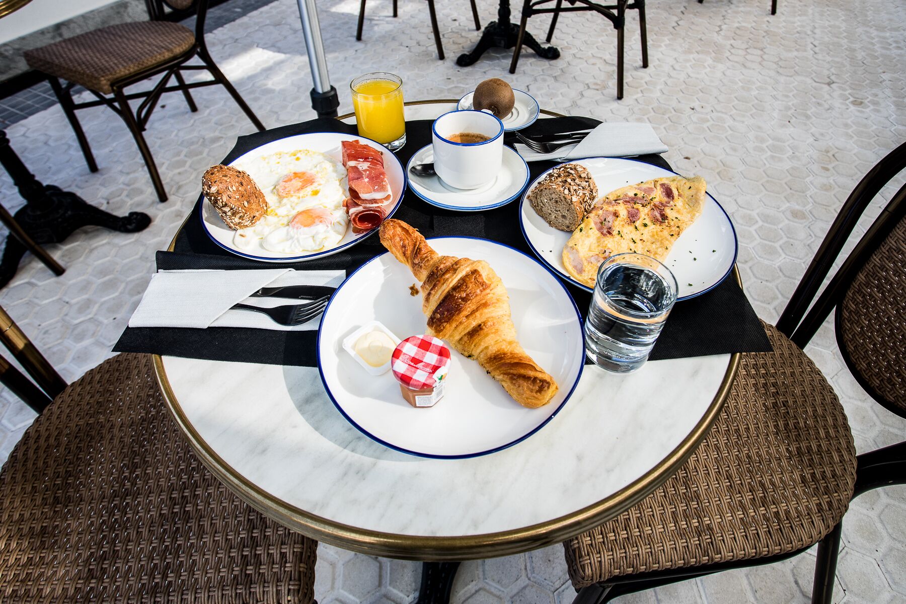 A breakfast setting with croissants, eggs, ham, and a croissant with butter on a marble table.