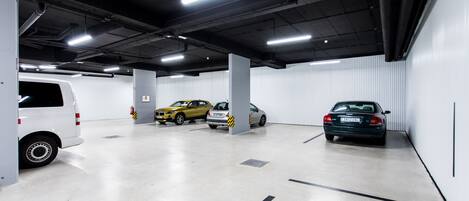 Un estacionamiento con paredes blancas, pisos de concreto e iluminación fluorescente en el techo.
