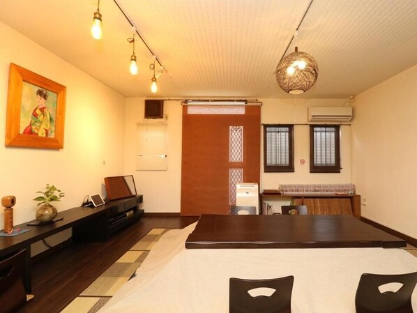A traditional Japanese-style room with tatami flooring, a low table with a laptop, a piano, and a hanging light fixture.