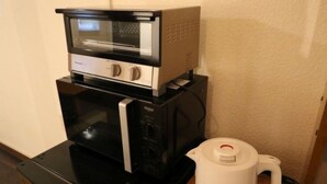 A kitchen with a microwave, toaster oven, and a white electric kettle on a black countertop. - Guesthouse Kyoto Yamashina (Kyoto)