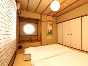 Una habitación tradicional japonesa con suelo de tatami, futón, puertas correderas y un biombó shoji.