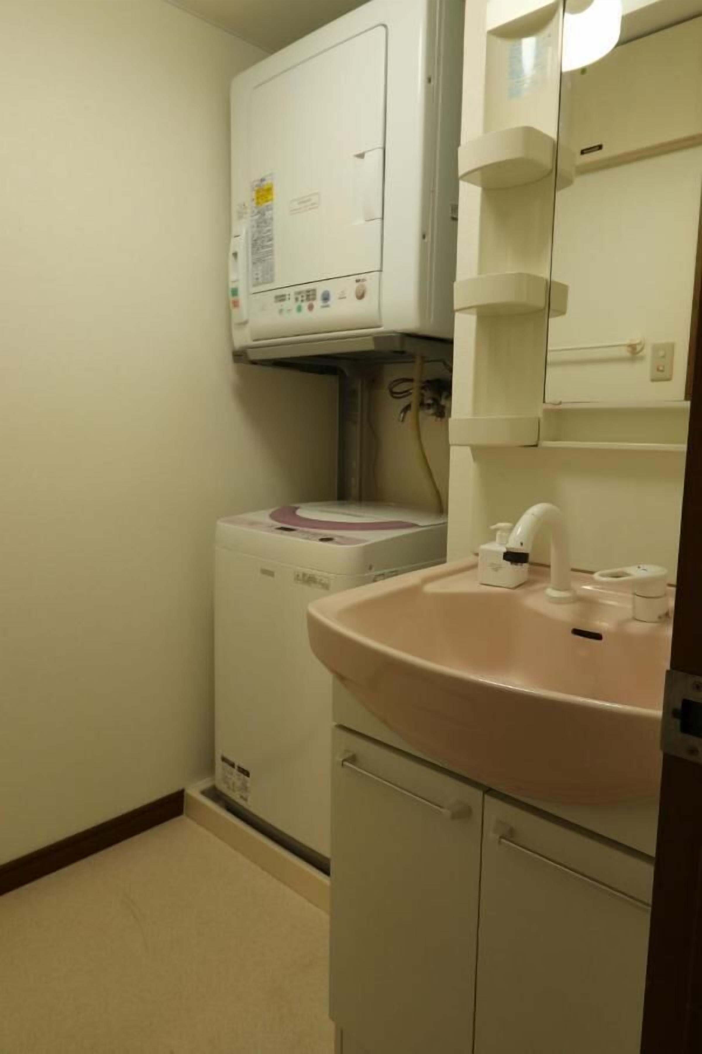 Une petite salle de bain avec un lave-linge blanc, un lavabo rose et un miroir au-dessus.