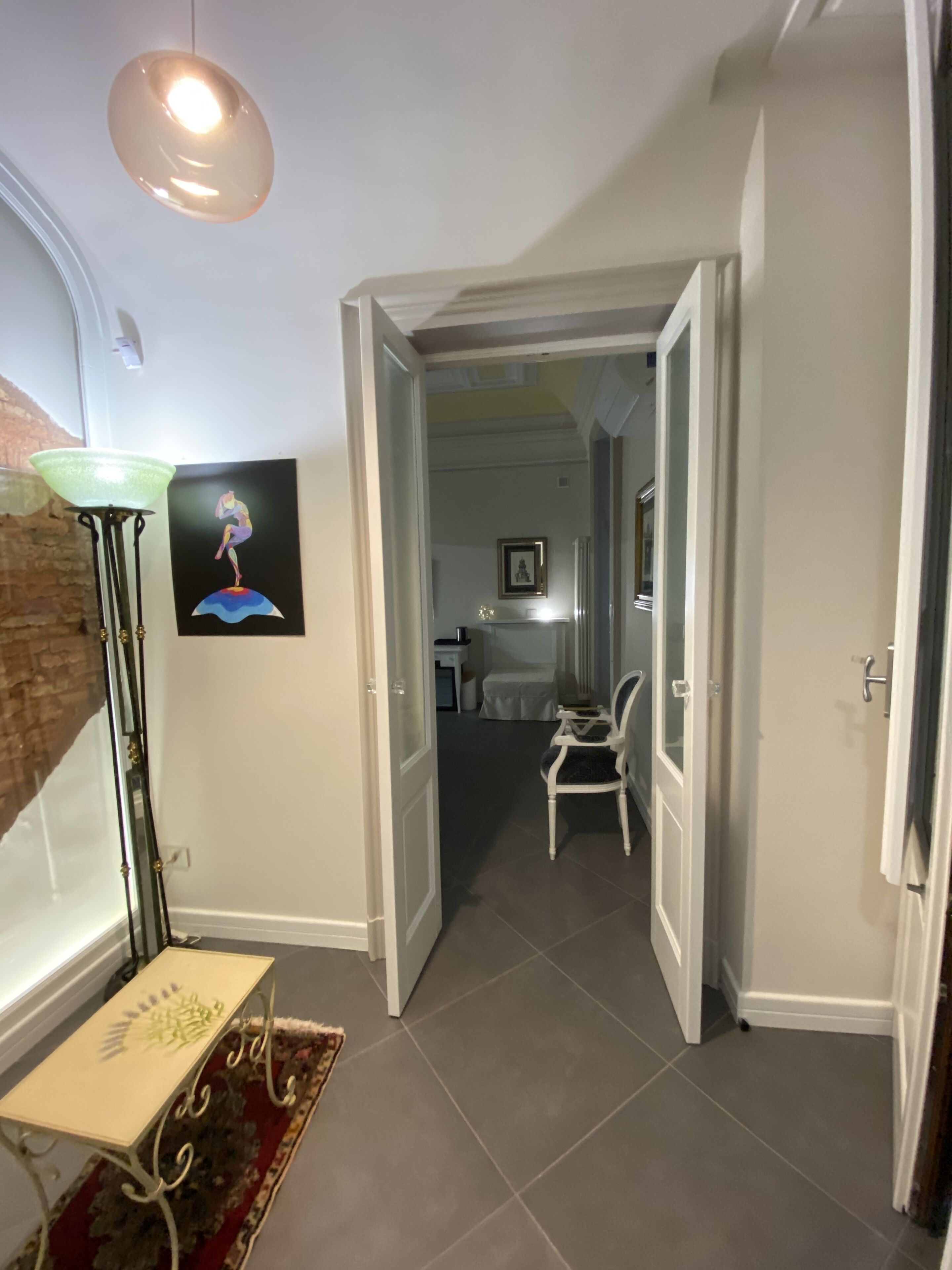 A hallway with a white chair, a framed artwork, and a table with a patterned table runner.