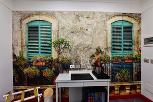 Habitación con un mural de un balcón, un escritorio blanco y un refrigerador.