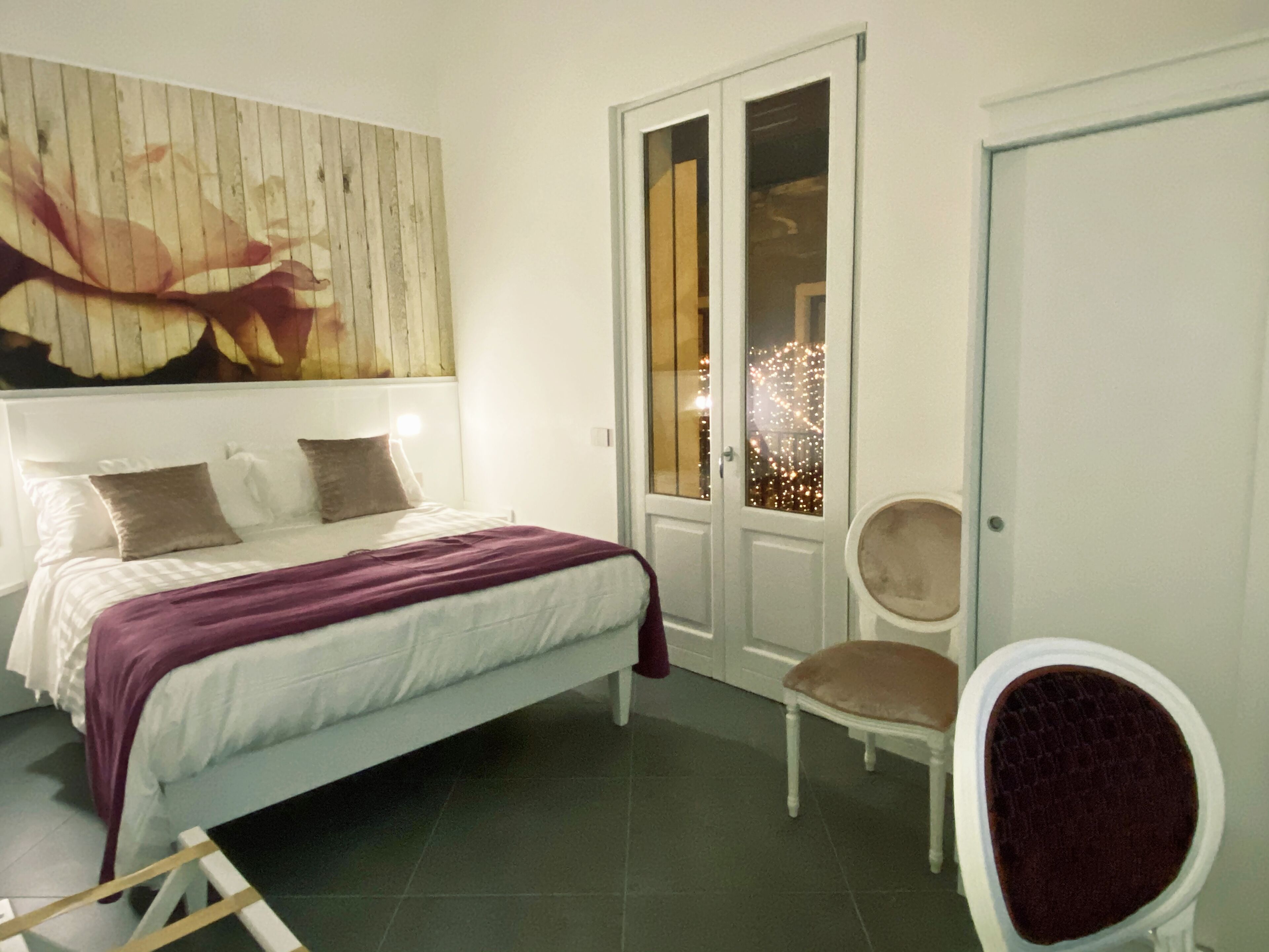 A bedroom with a bed, a chair, a door, and a wall with a painting.