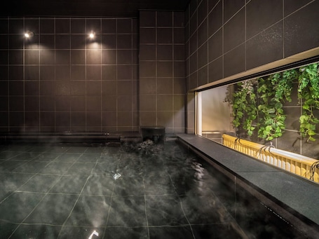 A spa area with a hot tub, tiled walls, and a view of greenery through a window.